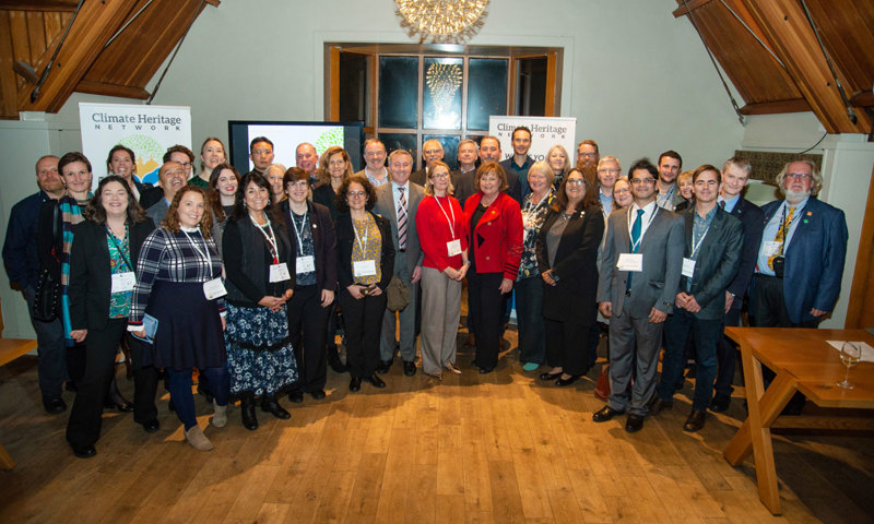 A large group of people stand together in a room with a wooden room, wearing lanyards and smiling at the camera.