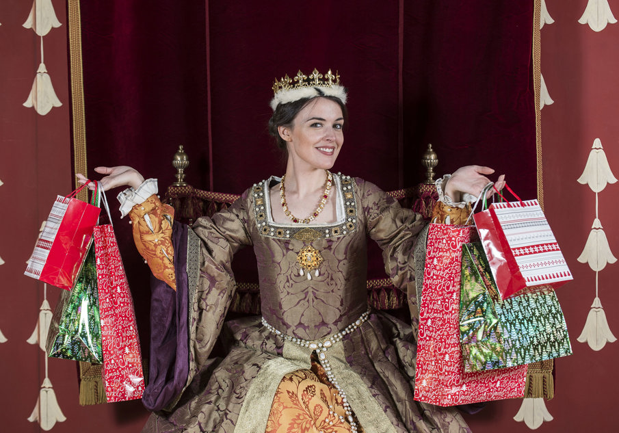 Model dressed as Queen sitting on throne holding up bags of presents