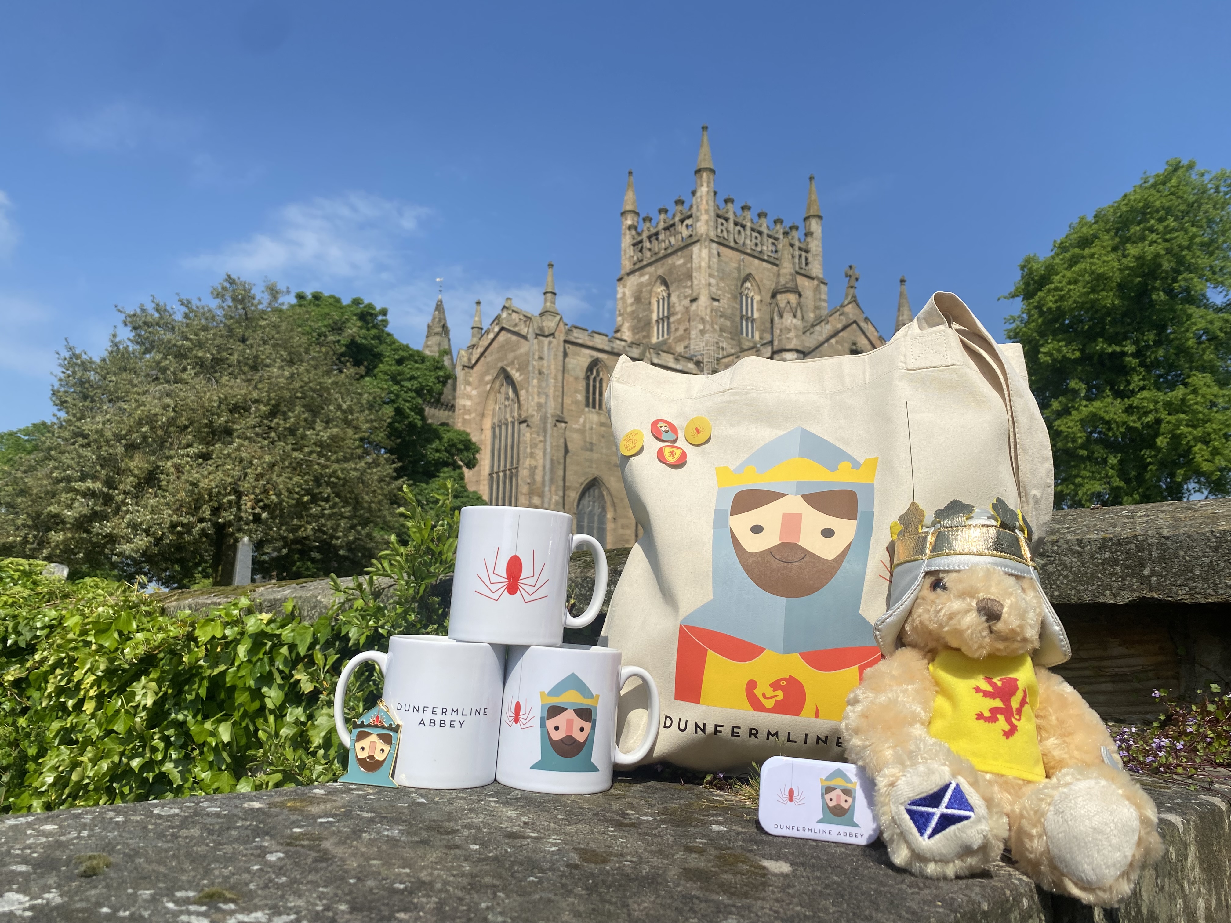 Robert the Bruce merchandise with an abbey building, trees and blue sky behind them.