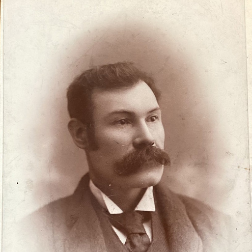 Old, sepia-toned portrait photograph of Andrew Baird. He is well dressed with dark hair and a large moustache.
