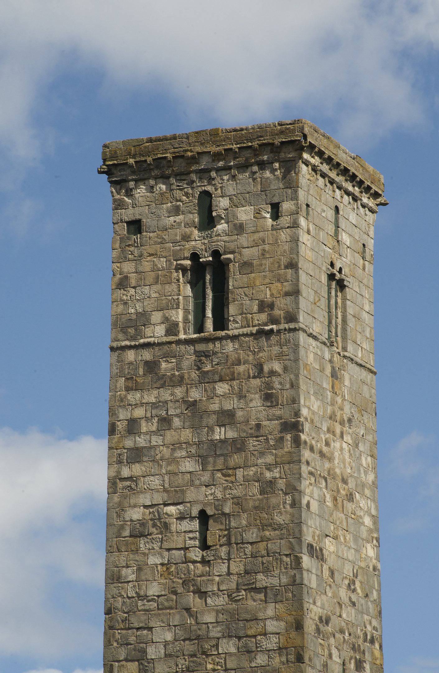 A close-up photo of an imposing square stone tower with small windows towards the top