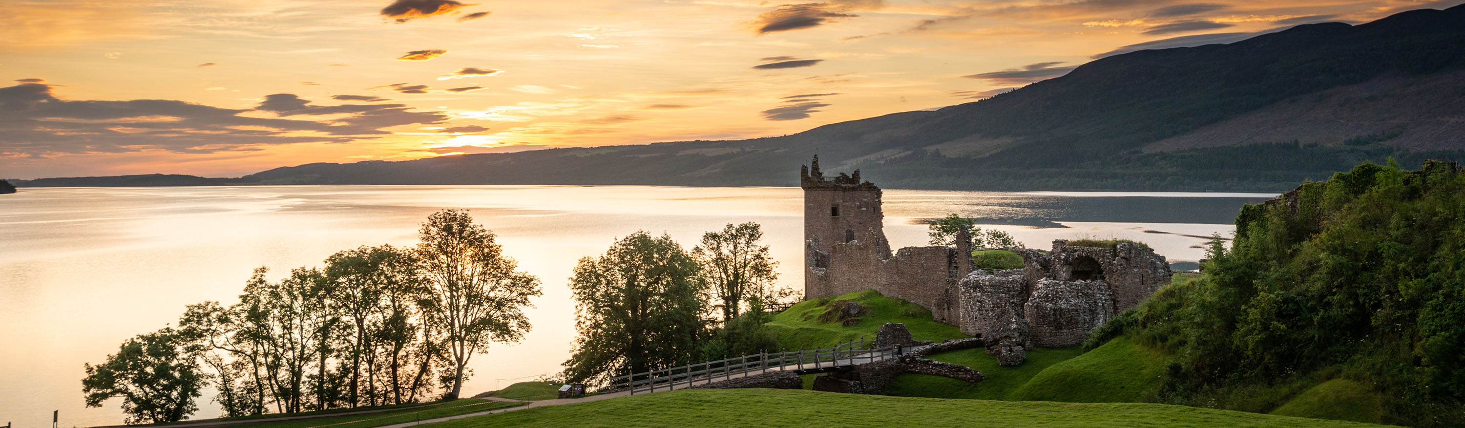 A dramatic skyline at sunset with castle ruins and a loch bathing in the last of the light