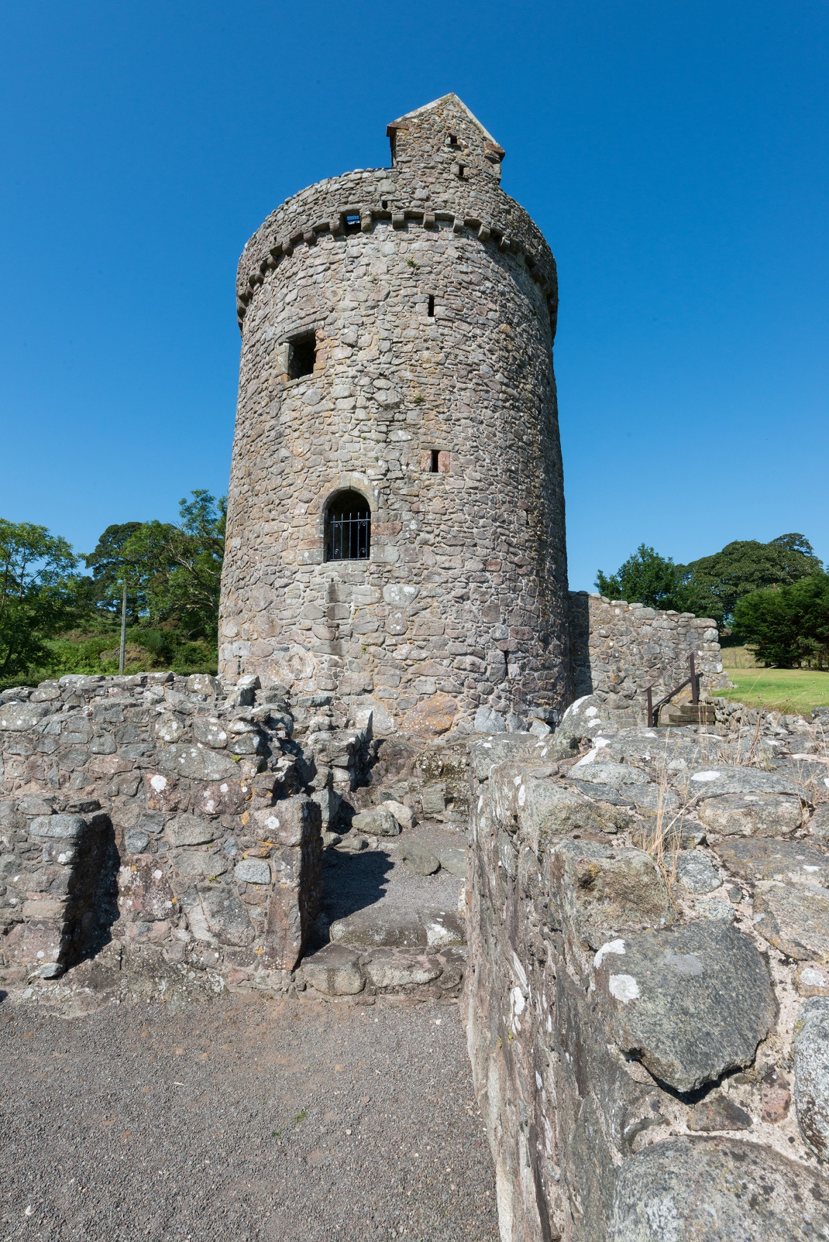 Orchardton Tower viewed from within low stone ruins in the foreground, emphasising the height and circular form of the tower.