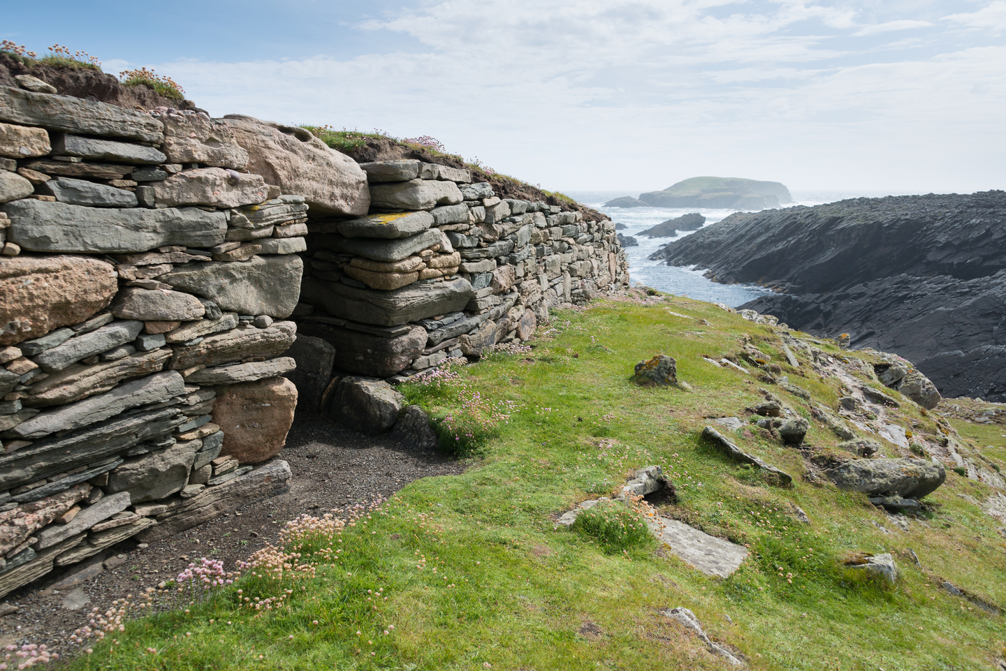 Entrance of a stone building, with the sea and cliffs in the background. 