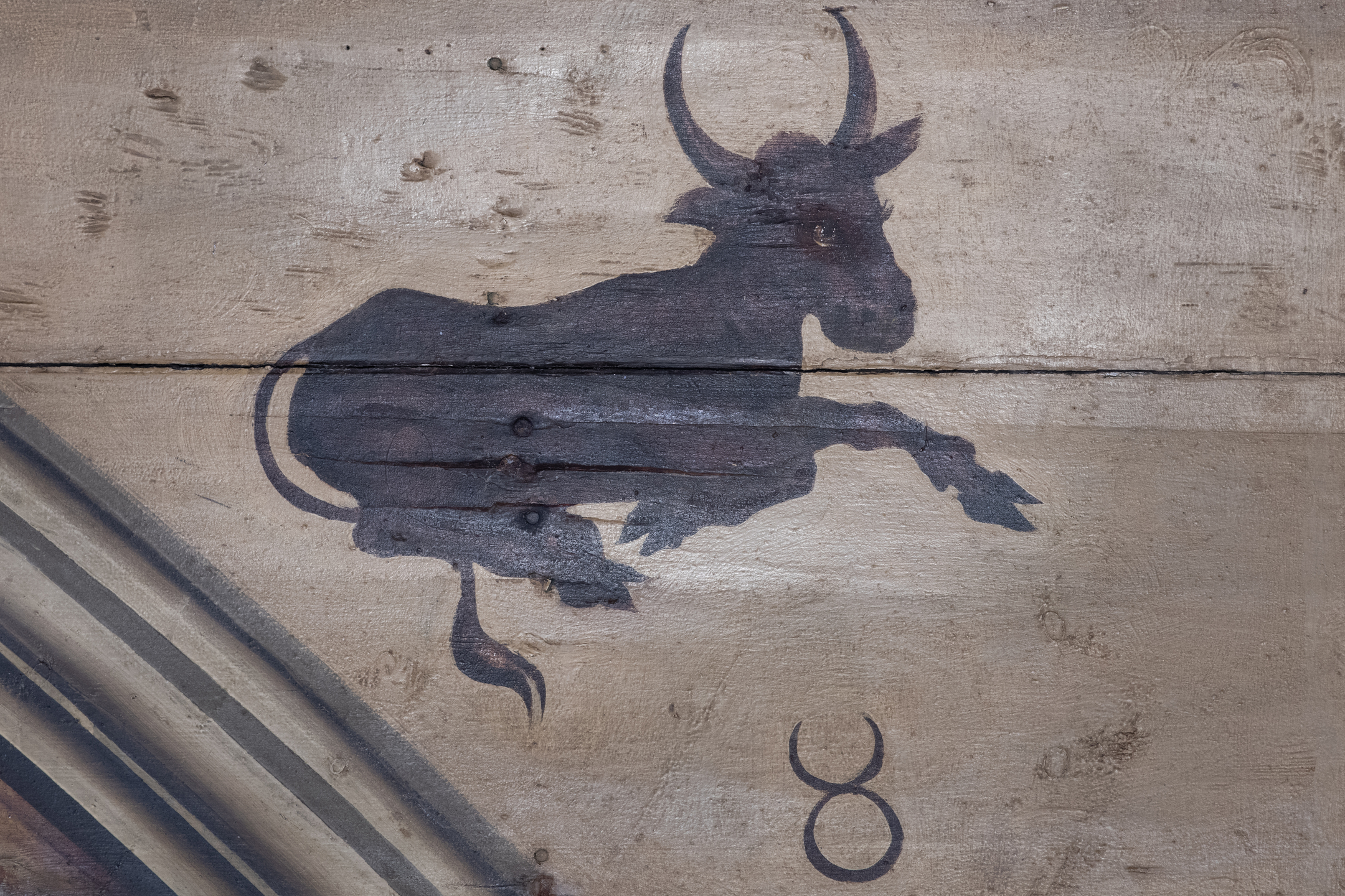 Painting on wooden ceiling boards showing a stylised dark bull in mid-leap, with curved horns and a tail, positioned above the Taurus zodiac symbol.