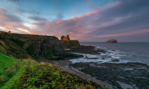 Distant view of Tantallon Castle with red sky above and Forth Estuary