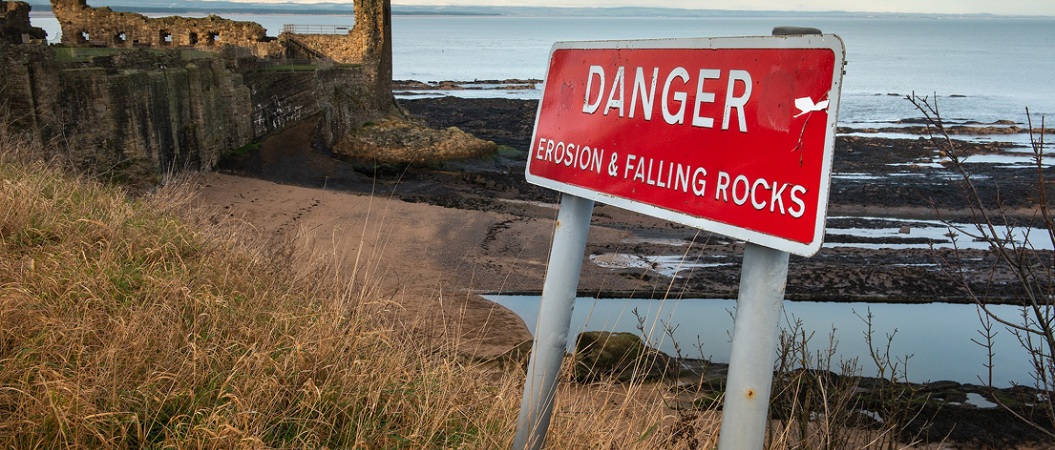 A sign on the coast by a castle which reads "Danger, falling rocks"
