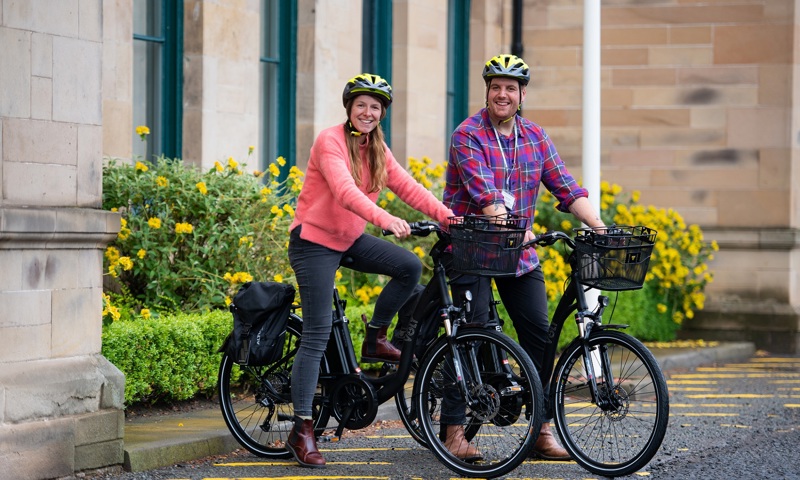 Two people sitting on bikes outside a historic building