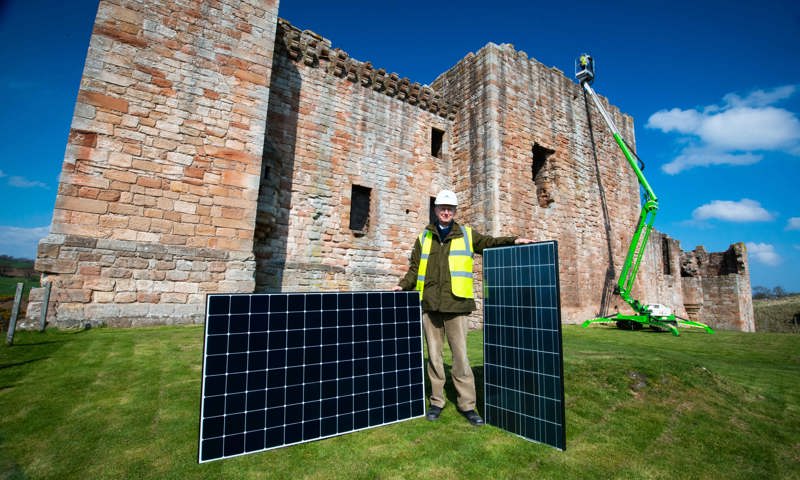 A person standing outside a historic castle with two large solar panels