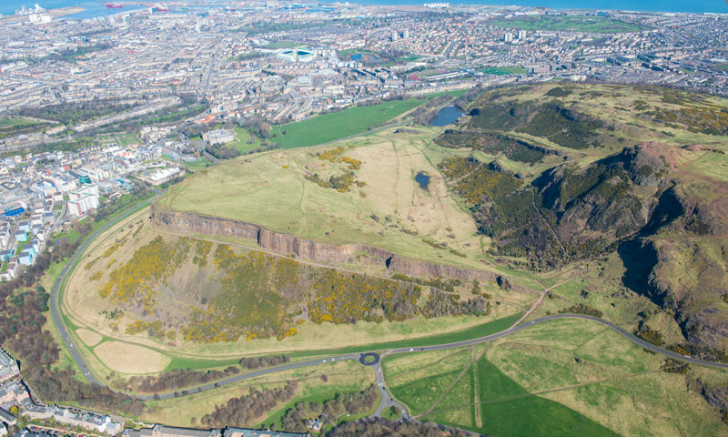 An aerial photograph of a large hill with a road running around it.
