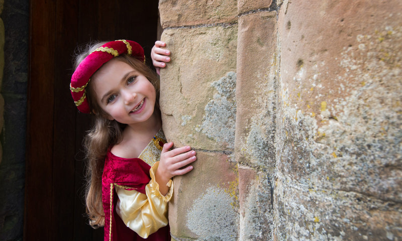 Girl in costume with a big smile, peaking out from behind a wall at a castle