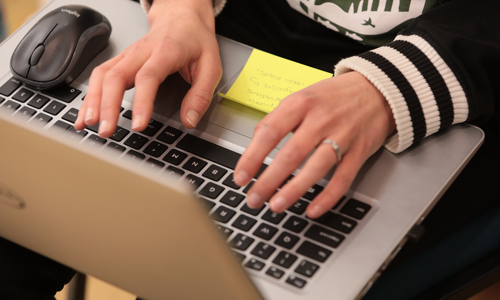 A person sits with a laptop on their lap and types