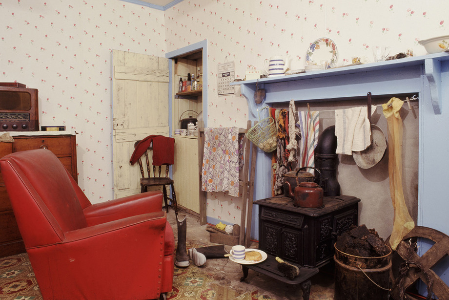 A 1950's kitchen with a red chair and blue fireplace, and black iron stove
