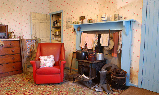 A 1950's kitchen with a red chair and blue fireplace, and black iron stove