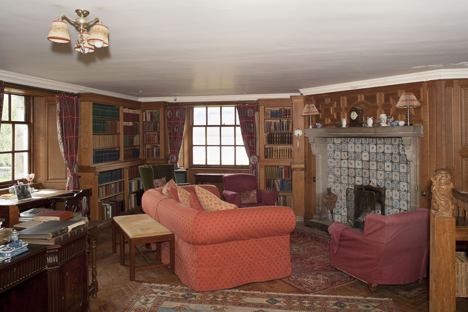 A room clad with wooden walls, filled with books, armchairs, desks and tables