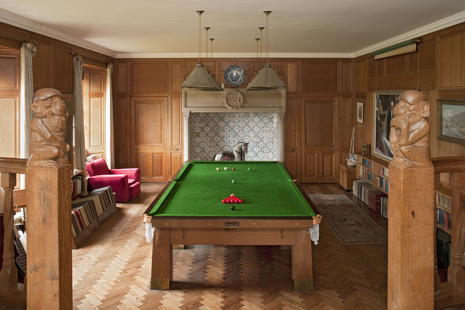 A room with a billiard table in the centre. The room's walls are clad in wood.