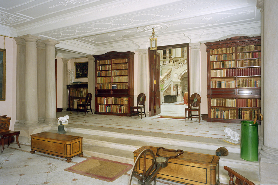 A room with floor-to-ceiling bookcases, a decorative plaster ceiling, and chairs