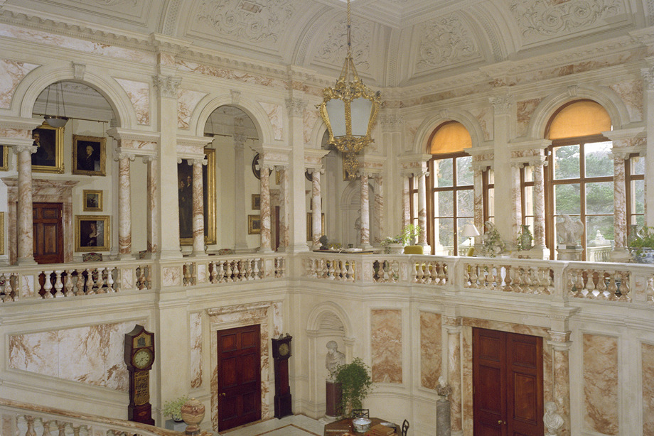 A marble hall with large, arched windows and a gold, pendant light