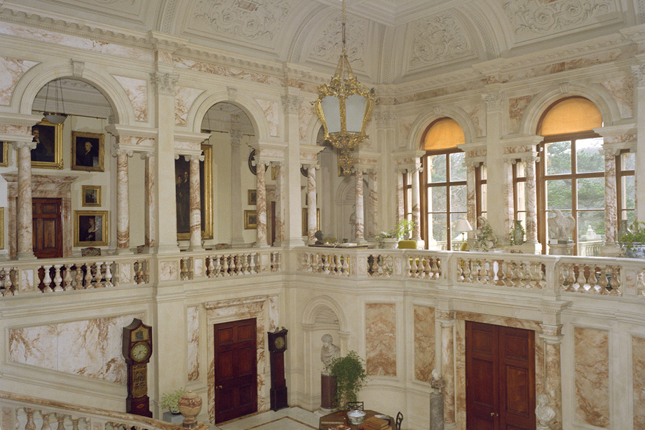 A marble hall with large, arched windows and a gold, pendant light