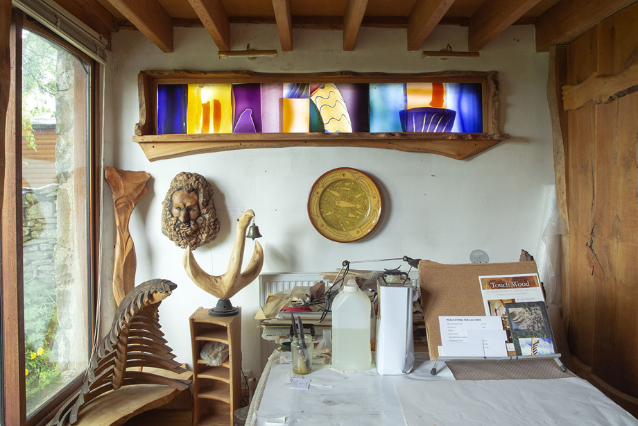 A long, narrow, abstract stained glass window in a room with wooden sculptures