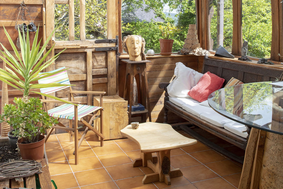 A wooden and glass conservatory, with carved wooden furniture and sculptures