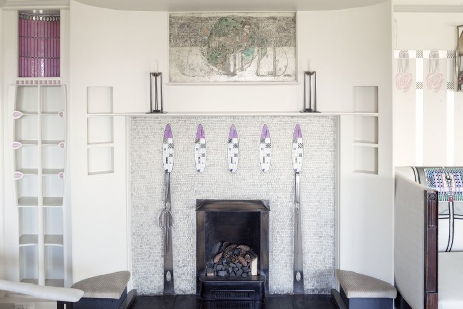 A white mosiac fireplace with floral mosiac designs, and a gesso painting above the fireplace