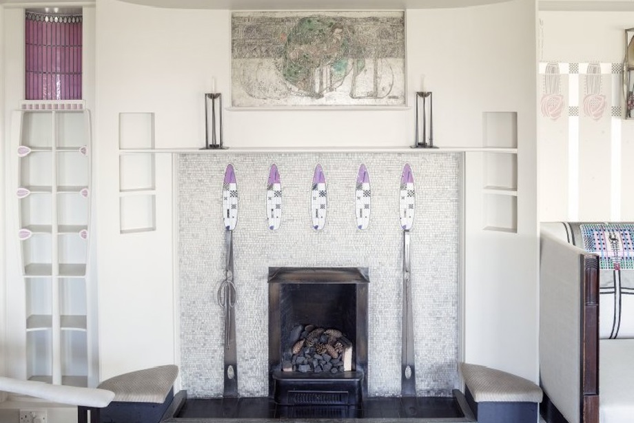 A white mosiac fireplace with floral mosiac designs, and a gesso painting above the fireplace
