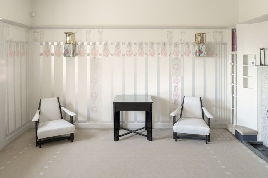 A room with decorative rose designs on the walls, and two white arm chairs flanking a small table