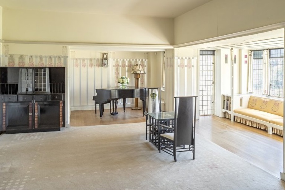 A drawing room with a dark wooden grand piano and furniture, and rose designs on the walls and furniture