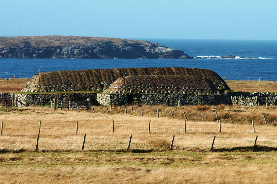 A pair of low thatched houses sit in fields beside the water