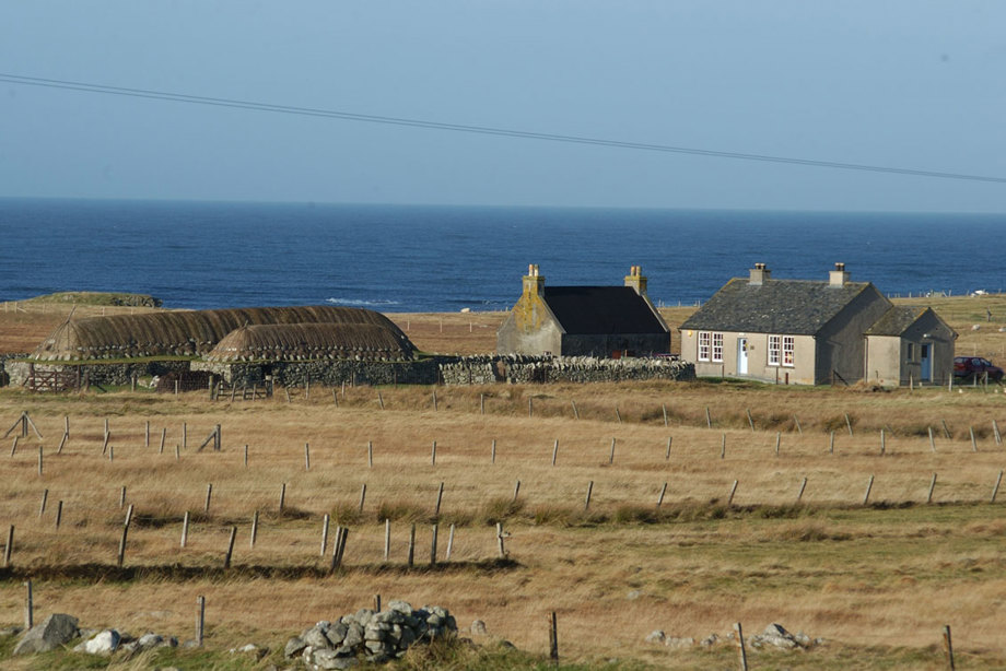 A pair of low thatched houses sit in fields beside more modern single storey houses