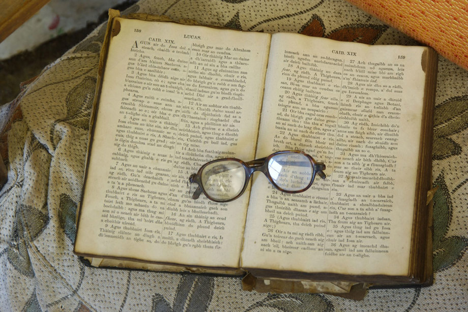 A pair of reading glasses sit on top of an open book written in Gaelic