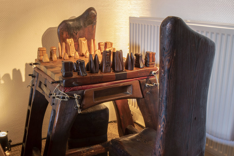 A carved wooden chess set, on a table with carved wooden chairs