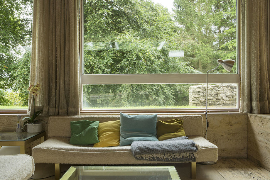 A seat covered with cushions and blankets, in front of a large window