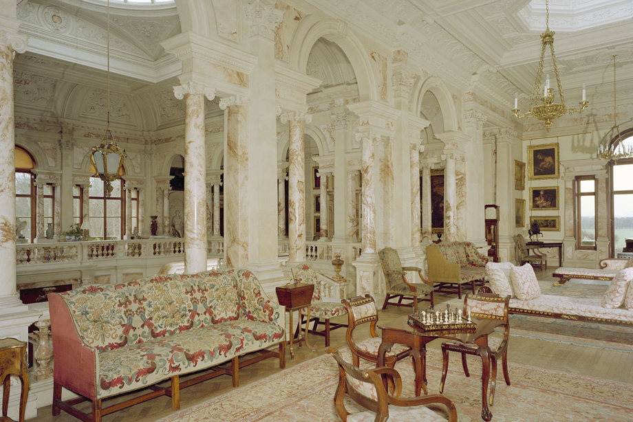 A large, marble hall with patterned and wooden furniture, and gold, drop ceiling lights