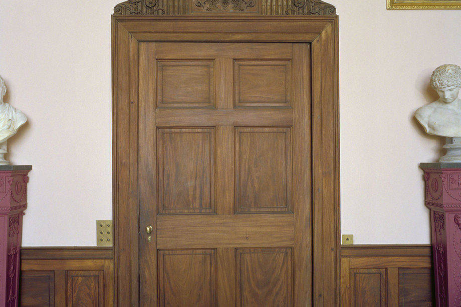 A large, wooden door, surrounded by paintings in gold frames