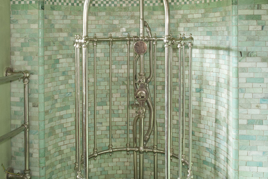 A green and white tiled room with a silver sculptured shower, with silver pipes featuring as an exposed cage around the shower