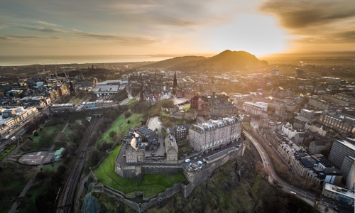 Aerial image of Edinburgh skyline at dawn. Edinburgh Castle is in the foreground and Arthur's Seat is behind.