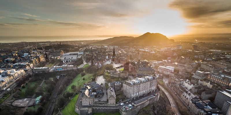 Aerial image of Edinburgh skyline at dawn. Edinburgh Castle is in the foreground and Arthur