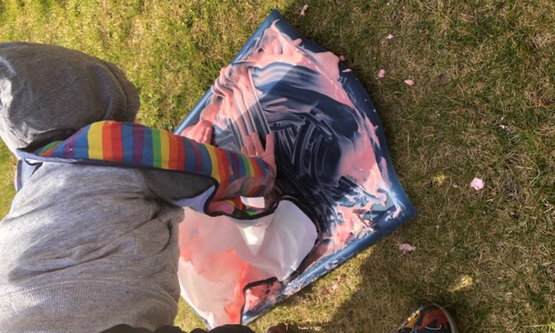 A child wearing an apron and outdoors, having a fun with yoghurt on a tray to make Mason