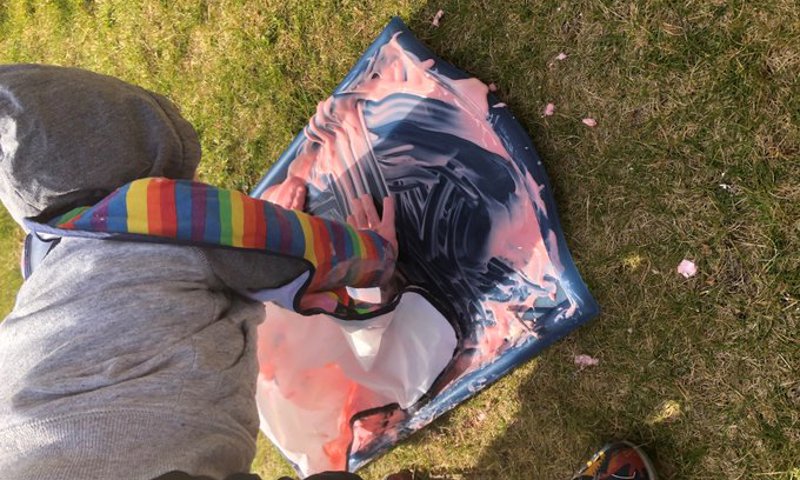 A child wearing an apron and outdoors, having a fun with yoghurt on a tray to make Mason