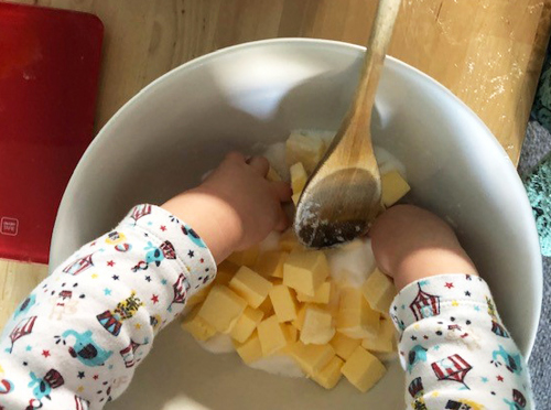 Child's hands in a mixing bowl with a wooden spoon, combining butter and sugar