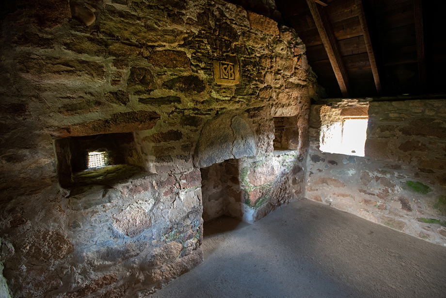 An empty stone room with intials carved above a fireplace