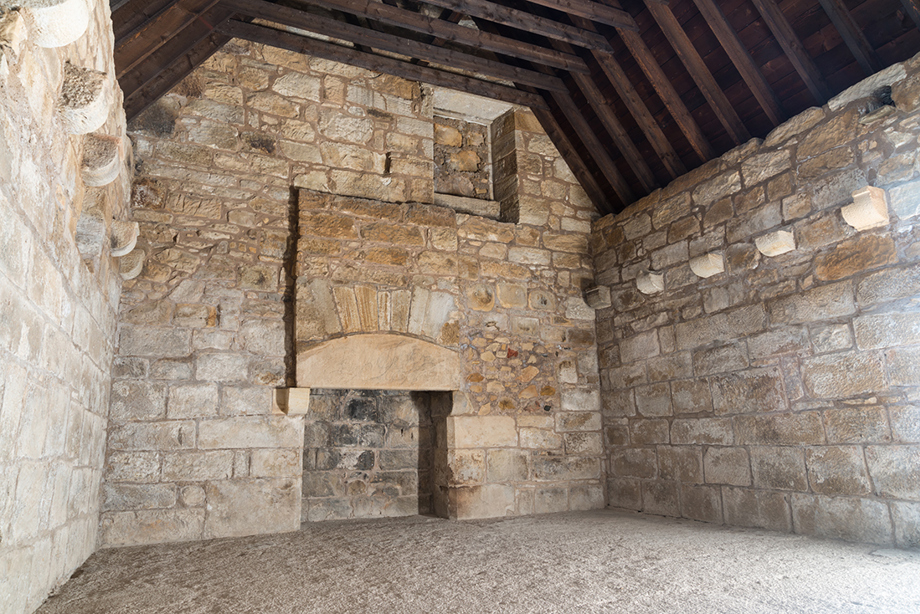A large room with stone walls, a timber roof and a massive fireplace