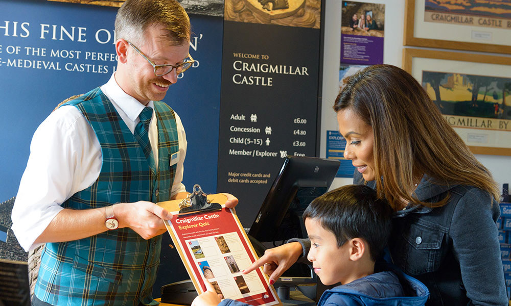 A steward on site showing a clipboard with a quiz on it to a woman and child