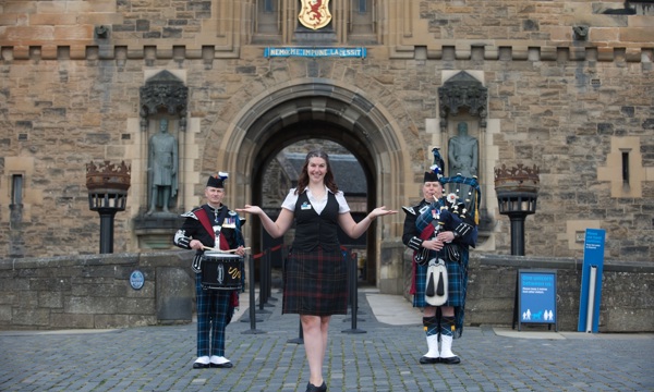 Edinburgh Castle guide stands in front of the main entrance flanked by two pipers.