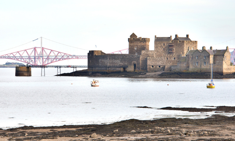 A distant view of Blackness Castle, with the Forth Rail Bridge behind it.