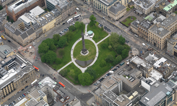 Bird's eye view of a tall monument in a green square in the centre of a city.