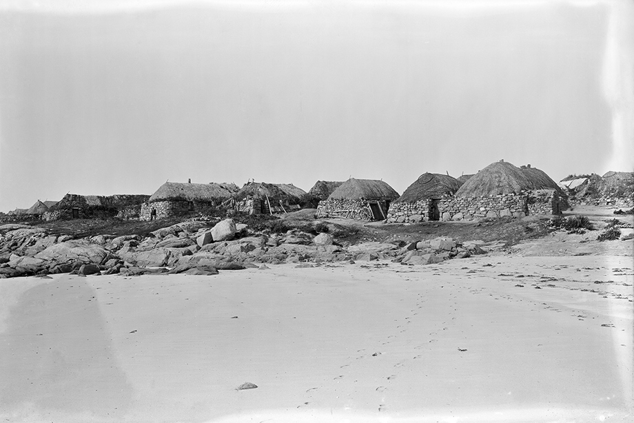 A series of low, thatched buildings on a sandy shore