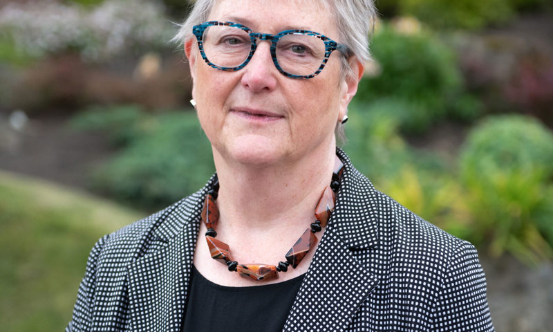 A woman wearing glasses and a formal jacket smiles at the camera